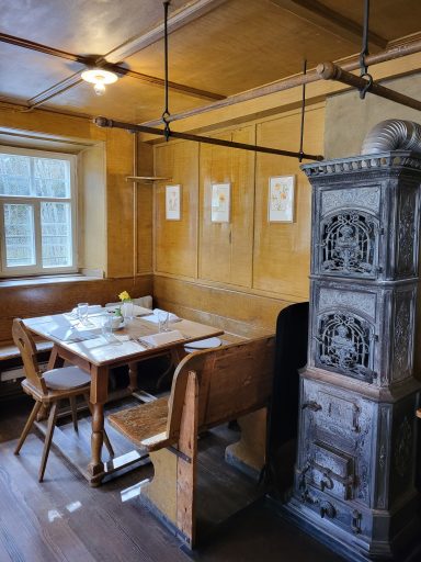 Blick in die Stube. Im Vordergrund der alte Ofen, dahinter die Ecksitzgruppe mit eingedeckten Tisch