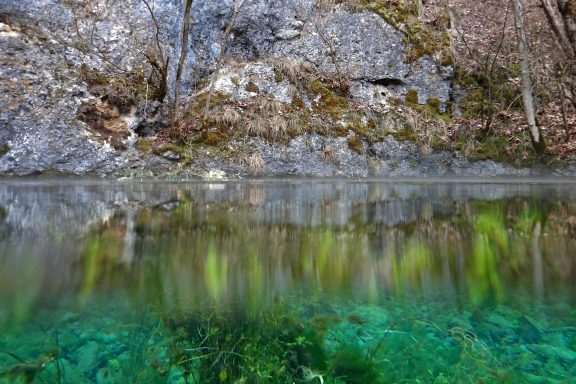 Bild von oben ins Wasser. Blau- und Grüntöne des Wassers, das aus dem Felsen unterirdisch aus dem Felsen kommt