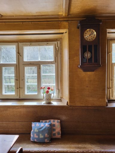 Blick in die Stube. Auf der Sitzbank zwei bunte Kissen und an der Wand eine alte Uhr aus Holz